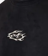 Remera de manga corta, cuello redondo y corte boxy, confeccionada en gamuza sintética (suede) de color negro. Presenta una pequeña estampa localizada en el pecho con un diseño abstracto en tonos dorados/bronce.