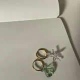 Par de aros dorados tipo argolla con dijes de vidrio colgantes: uno con forma de estrella de mar rosa y otro con forma de concha verde.