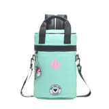 Mochila térmica cilíndrica color verde menta, acolchada con efecto puffer y acabado brillante. Presenta tiras negras de cuero sintético para llevar como mochila o bandolera, y detalles decorativos como un parche rosa con dos barras verticales y un parche circular con texto. Incluye un llavero colgante con forma de flor multicolor.