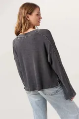 Remera de manga larga con escote en V amplio, confeccionada en tejido térmico suave con lavado burnout que le da un acabado vintage. Presenta costuras expuestas y bordes sin rematar, con mangas levemente acampanadas.