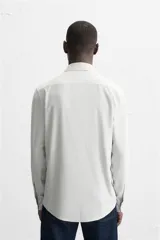 Camisa celeste a rayas verticales blancas, de corte recto, con cuello italiano abierto, mangas largas con puños abotonados y cierre frontal con botones.