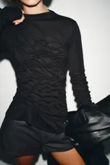 Top negro de cuello perkins y manga larga con frunces en el pecho y las mangas.