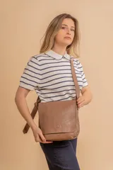 Bandolera de hombro color gris claro, con solapa frontal y correa ajustable. Presenta un diseño simple y práctico, ideal para uso diario.