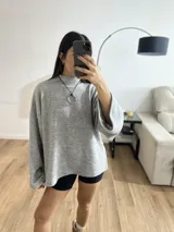 Sweater gris de tejido de punto grueso, con cuello alto, mangas anchas y aberturas laterales.