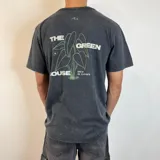 Remera gris con efecto gastado, corte clásico y estampa en la espalda con la frase "The Green House" y un dibujo de una planta oreja de elefante.