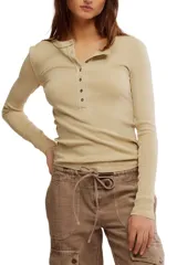 Camiseta tipo henley de manga larga, color beige claro, confeccionada en tejido acanalado. Presenta un escote con tapeta de botones y costuras deshilachadas en los bordes.