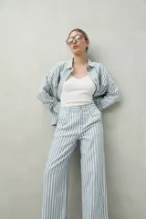 Pantalón de lino a rayas verticales azules y blancas, de corte amplio y relajado, con bolsillos laterales y cierre frontal con botón.