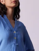 Túnica celeste de algodón con escote en V y detalle de puntilla. Tiene mangas largas con puños abotonados y cierre frontal con botones.