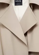 Trench color beige con solapas, trabillas en los hombros y puños, cinturón desmontable y bolsillos laterales.