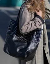 Bolso tote negro con tachas plateadas y doble asa de hombro.
