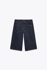 Bermuda de jean azul oscuro, tiro medio, con cinco bolsillos, trabillas en la cintura y pespuntes marcados a contraste.