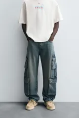 Pantalón de denim color beige, corte relaxed fit, con bolsillos laterales tipo cargo con solapa y cierre de botón. Cierre frontal con botón y cremallera.