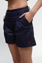 Short de jean azul oscuro con pespuntes rojos, tiro medio/alto, bolsillos delanteros y traseros al estilo jean y tablones delanteros.