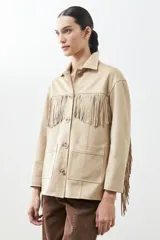 Chaqueta color beige de simil gamuza con flecos en mangas y ruedo, con cuello camisero y cierre frontal con botones.