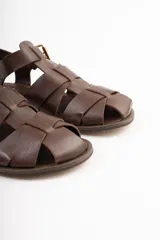 Sandalias bajas de cuero marrón con tiras entrecruzadas y hebilla dorada.