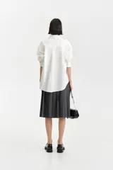 Camisa blanca de algodón con corte amplio y abotonadura frontal. Presenta un pequeño detalle bordado en un costado del frente.