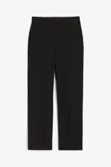 Pantalón de vestir negro con cintura elástica, bolsillos al bies y piernas ajustadas con pliegues. Cierre con corchete y botón ocultos.