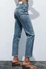 Pantalón de jean gris oscuro, de corte mom fit, tiro alto y largo tobillero. Cuenta con cinco bolsillos, cierre frontal con cremallera y botón.