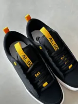 Championes CIRCA 50 PRO EVOLUTION, color negro con detalles en amarillo, de caña baja, con triple costura en la puntera, lengüeta acolchada, cordones ocultos y suela de goma FusionGrip™ vulcanizada.