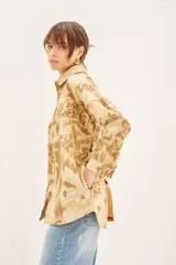 Campera de corte recto confeccionada en gabardina estampada con bordados de hilo. Presenta cuello camisero, cierre frontal con botones, dos bolsillos de parche con solapa en el pecho y lazo ajustable en la cintura con detalle bordado.