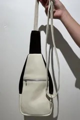 Mochila bandolera de cuero color marrón chocolate y detalles en color crema. Tiene dos bolsillos con cierre y correa regulable.