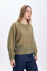 Camisa casual manga larga color verde oliva, de tela traslúcida con textura sutil. Tiene cuello redondo, cierre frontal con botones y mangas largas con puños elásticos.