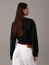 Buzo negro de felpa con cuello redondo y logo Calvin Klein Jeans estampado en el pecho. Tiene ribetes rojos en el cuello y en el ruedo.