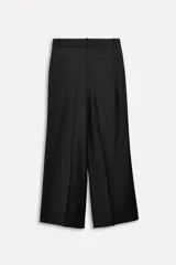 Pantalón negro de tiro alto con trabillas, confeccionado en mezcla de lana. Presenta bolsillos laterales, falsos bolsillos de doble vivo, cinturilla interior a contraste con pespuntes y raya planchada en el delantero. Cierre frontal con cremallera, botón interior y ganchos metálicos.