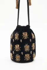 Cartera tipo bombonera negra de terciopelo con bordado de lentejuelas y canutillos dorados con forma de insectos. Tiene cordón de ajuste con borlas de canutillos dorados y correa de mano.