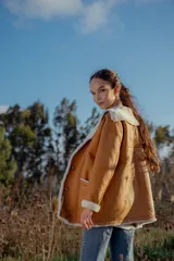 Campera gamulan color camel de cuero italiano con interior de piel sintética blanca. Tiene cuello solapa amplio, cierre con botones y bolsillos laterales.