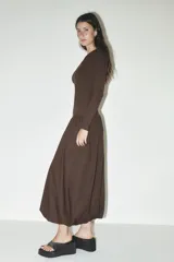 Vestido midi marrón de escote asimétrico con un hombro descubierto y una manga larga. La falda es amplia con bolsillos laterales y bajo tipo globo.