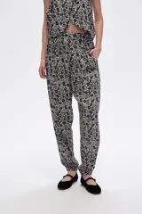 Pantalón slouchy de viscosa con estampado floral en tonos beige y negro, bolsillos laterales, cintura alta y detalle de punto smock en los tobillos.