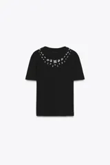 Camiseta negra de manga corta y cuello redondo con apliques de strass y cuentas plateadas alrededor del cuello.