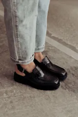 Zueco negro con textura croco, diseño tipo mocasín y tira regulable al talón.