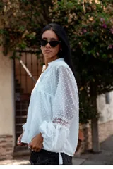 Camisa blanca de plumetí con cuello mao, mangas largas abullonadas con puños elásticos y cordón con borlas en el escote.