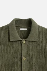 Camisa verde militar de punto con estructura abierta, corte regular fit, cuello solapa, manga corta y cierre frontal con botones.