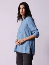 Blusa celeste en lyocell, con cuello a la base con solapa, escote en V y abertura central con botones. Manga larga regulable con presilla y botón.