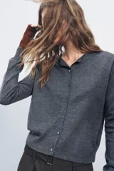 Chaqueta de punto fino color gris oscuro confeccionada con lana. Tiene cuello redondo, manga larga y cierre frontal con botones.