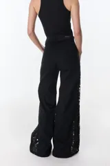 Pantalón de jean negro de pierna ancha con cortes en los laterales que van desde la pretina al bajo del pantalón. Por la mitad de la pierna presenta godets triangulares de encaje para darle mayor amplitud y detalles a la prenda.