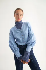 Blusa celeste de escote en V, con botonadura frontal cruzada y mangas largas abullonadas con puños ajustados.