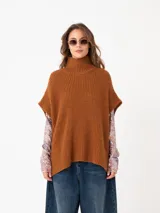 Chaleco tipo poncho confeccionado en tejido grueso de punto color tostado. Presenta un diseño holgado sin mangas con cuello alto tipo polera, ideal para el invierno.