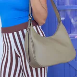 Cartera negra ovalada de simil cuero con cierre y correa ajustable con ojales. Cuenta con bolsillos internos y un bolsillo trasero.