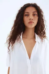 Camisa blanca de viscosa con efecto arrugado, de manga corta, corte holgado, cuello clásico, botones frontales y canesú con pliegue de caja en la espalda.