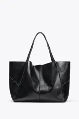 Bolso maxi shopper de cuero negro con pespuntes a tono. Tiene asas de hombro y cierre con tiras y botón. Incluye una cartera con bolsillo extraíble.