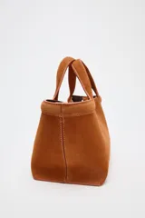 Bolso mini shopper color marrón de serraje, con asa de mano y asa bandolera extraíble. Tiene detalle de pespunte en el corte, bolsillo interior y cierre mediante mosquetón.