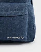Mochila azul de denim con bolsillo frontal con cierre y tirador con charms decorativos. Tiene correas regulables, manija superior y cierre superior.