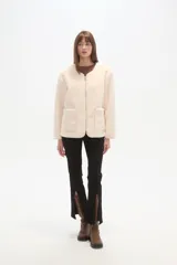 Chaqueta corta de tejido bouclé o pelo sintético color crema, con cuello redondo, cierre frontal metálico y dos bolsillos frontales amplios.