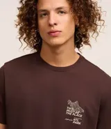 Remera marrón de algodón peruano, corte comfort, cuello redondo, manga corta y estampa frontal con texto y dibujo.