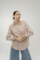 Camisa blanca de lino con cuello clásico, cierre frontal con botones y manga larga. Presenta detalles de crochet en cuello, puños y bolsillo.