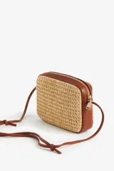 Cartera bandolera rectangular de paja color beige, con detalles y correa fina ajustable de cuero marrón.